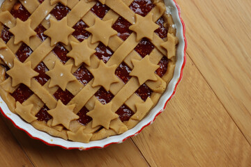 Tart with dark fig jam in a white ceramic cake pan on wooden table ready to be baked 