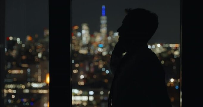 Silhouette of a man talking on the phone angry or upset, walking back and forth Manhattan view in background. Handheld camera slowly moving. Man expresses his frustration and anger. City night lights.