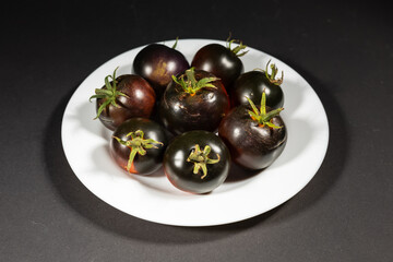 Ripe tomatoes in a white plate on a black background. Black tomatoes. Cumato tomatoes