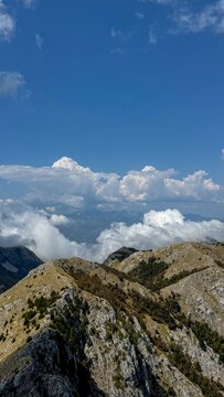 A wide view of a rugged mountain ridge, with rocky outcrops and sparse vegetation, set under a vast, cloud-filled blue sky.
