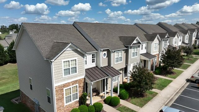 Aerial of modern row of houses with porch in suburb district. American town during sunny day with clouds. New developed residential area in USA. Close up drone shot.