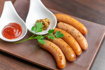 パリッと香ばしく焼き上げた「ソーセージのグリル」。ケチャップと粒マスタードを添えたジューシーな一皿は、居酒屋のスピードメニュー紹介や、ビールに合うおつまみ広告、キャンプ・BBQの料理イメージに最適な高品質素材です。 | Grilled sausages with ketchup and mustard on a plate.