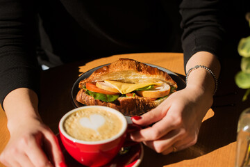 A woman drinks coffee with a croissant