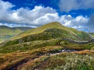 Rolling hills covered with green and golden grass under a dramatic sky with scattered clouds