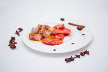 Savory bacon-wrapped tomatoes on a white plate.