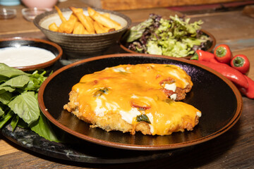A delicious plate of Chicken Parmo surrounded by the ingredients and classic British chips or fries on a wooden kitchen table