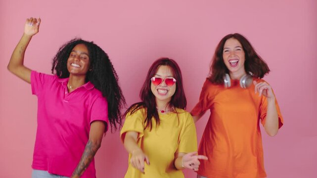 Trendy young women dance joyfully against a vibrant pink background, showcasing their colorful outfits and radiating energy, embodying celebration, friendship, and youthful spirit