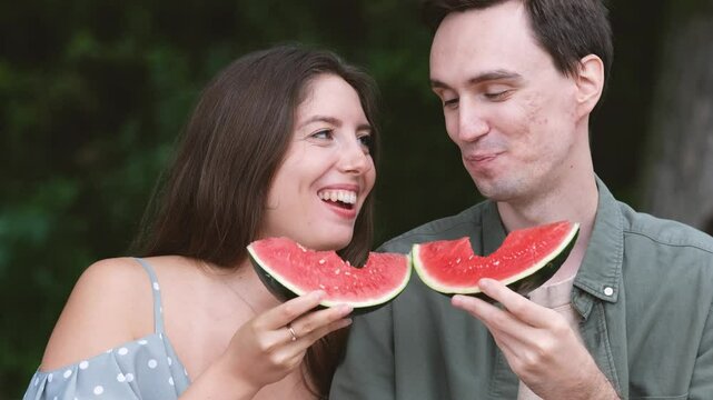 Smiling girl and guy eating juicy red watermelon outdoors