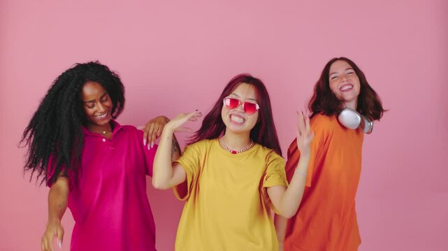 Three close friends joyfully celebrate life, adorned in vibrant and colorful attire, dancing animatedly together against a lively pink backdrop, truly embodying friendship and pure fun