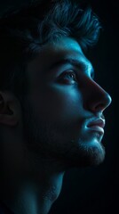 A creative headshot of a man with a dark, moody background, only half of his face illuminated by a soft light