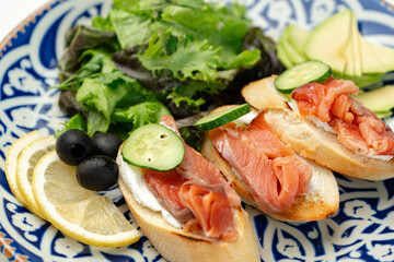 Colorful plate of smoked salmon sandwiches with cucumbers, greens, and olives on a decorative blue platter