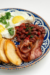 Delicious breakfast plate featuring eggs, beans, bacon, and potato wedges served on a decorative dish