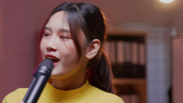 Asian woman singing passionately in a home office, showcasing her talent and joy while holding a microphone