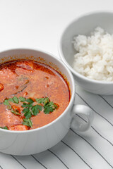 Bowl of curry with pieces of meat and a side of steamed rice arranged neatly for a meal