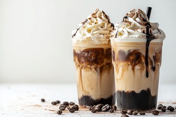 Two Iced Coffee Drinks with Whipped Cream, Chocolate Sauce, and Coffee Beans on White Background