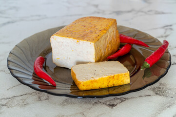 Smoked tofu sits on a plate with a pepper and a slice of tofu. The plate is on a marble countertop