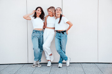 Three young beautiful smiling hipster female in trendy summer white t-shirt  and jeans clothes. Sexy carefree women posing in the street. Positive models having fun, talking, chatting. Going crazy