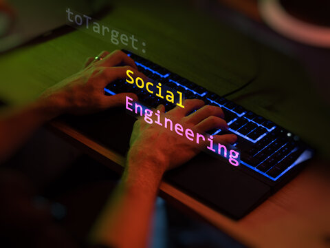 Social engineering text in foreground screen, hands of a anonymous hacker on a led keyboard. Vulnerability text in informatic system style, code on editor screen. Text in English.