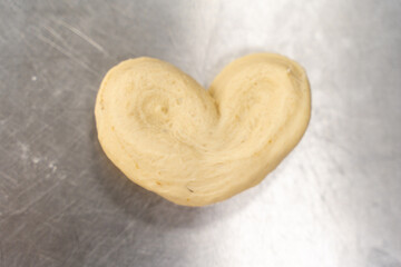 Heart-shaped dough on the production table. A blank for cookies or rolls in the kitchen. Space for text.