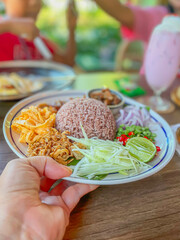 Closeup of shrimp paste fried rice thai food  held in a women hand with blurry background of people and dining atmosphere.