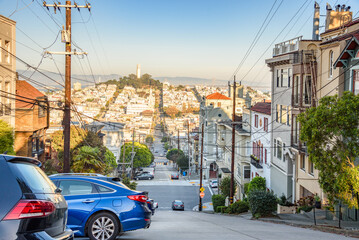 Steep street lined with apartment buildings and houses in a residential district of San Francisco on a clear autumn day. Coit Tower is visibile in distance.