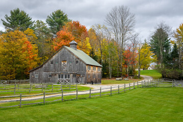 Old wooden barn with autumnal woods in background under stormy sky © alpegor