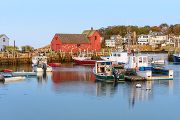 Obraz premium Fishing boats in harbour at twilight in autumn. A red wooden fishing shack on a stone quay is visible in background.