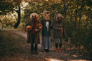 Three strange people in terrifying masks and odd clothes standing in autumn woods, creating creepy...