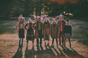 Group of people in creepy masks and odd clothes standing in autumn woods, creating terrifying atmosphere of holiday in vintage style. Concept of Halloween, spooky season, retro style.