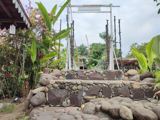 Stone path leading to a suspension bridge. The bridge is made of metal and rope, and it is...