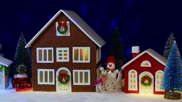Brown and red houses surrounded by a car, Christmas trees and a snowman on a sled on a dark blue background