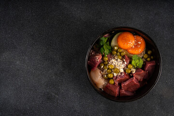 BARF (Biologically Appropriate Raw Food) food concept, Healthy bowl for domestic pets background with cat cute tabby kitten paws in pic.  Portion of raw meat, chicken, fish, vegetables, oats