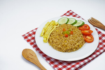 A plate of delicious fried rice served with sliced cucumber, tomato, and egg strips, placed on a red checkered cloth.