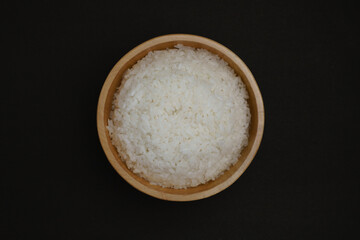Wooden bowl filled with white rice, on a black background. Perfect for culinary concepts, food presentations, or nutrition, photographed using a top angle