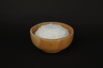 A wooden bowl filled with plain white rice, set on a black background. Perfect for culinary, food presentation, or nutrition concepts