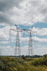 High voltage pylons against the blue sky with white clouds and bright green meadow. Power lines stretching into the distance. Perspective. Electricity