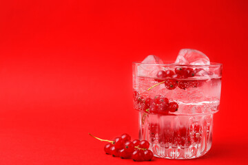 Refreshing water with red currants and mint in glass on red background, space for text