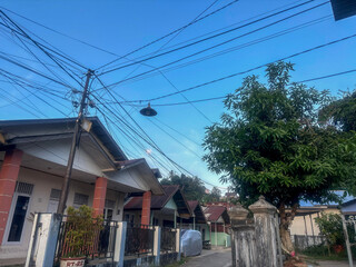 Obraz premium A portrait of a quiet village street with houses. The roofs of the houses have various shapes and colors. The electrical network above adds a sense of life to the image.