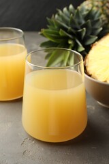 Tasty pineapple juice in glasses and fruits on grey textured table, closeup