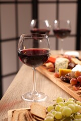 Glasses of red wine and different snacks on wooden table