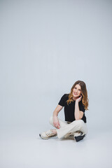 A pretty woman in a black t-shirt and white pants on a white background. Smiling woman in casual clothes on a white background.