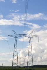 High voltage pylons against the blue sky with white clouds and bright green meadow. Power lines...