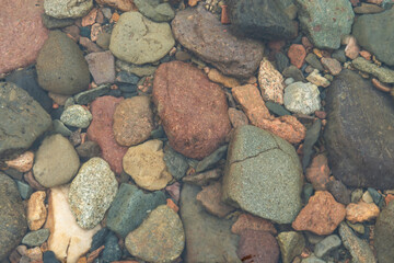 A shallow stream with rocks and pebbles on its bed. The water is crystal clear, allowing you to see the rocks and pebbles clearly. The rocks and pebbles vary in size and color, adding to the beauty of