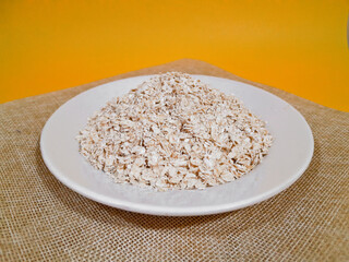 oat, oat grains, oat flakes in a white plate, isolated on yellow background and close up shot.
