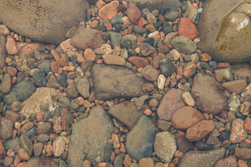 A shallow stream with rocks and pebbles on its bed. The water is crystal clear, allowing you to see the rocks and pebbles clearly. The rocks and pebbles vary in size and color, adding to the beauty of