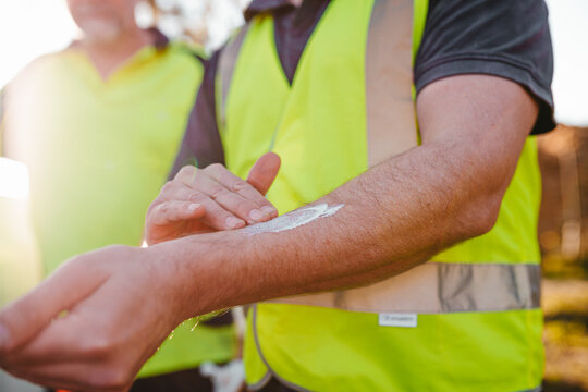 Construction worker on a blurry background rubbing sunscreen lotion on his arm.