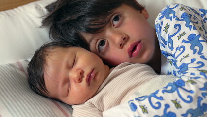 Sweet and tender moment as an older brother kisses his sleeping newborn sibling on the forehead, both lying on a bed, wrapped in warmth and love