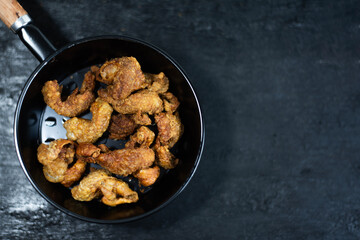 Fried chicken skin in a black pan on a black background