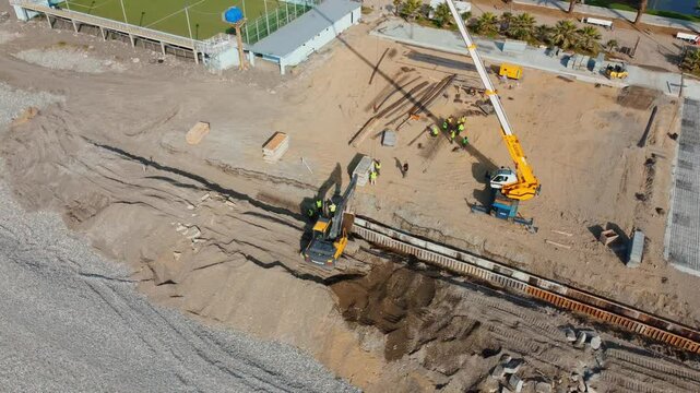 Batumi, Georgia - July 5, 2024.: Construction workers working on heavy machinery to build breakwater on beach. Excavators and cranes actively shape coastline, drone view.