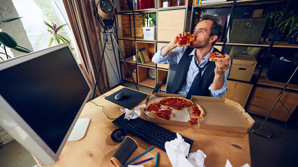 Man takes drink from bottle, holding his pizza slice, combining bad habits at workplace and reinforcing unhealthy approach to balancing work and breaks. Concept of people and daily work challenges.